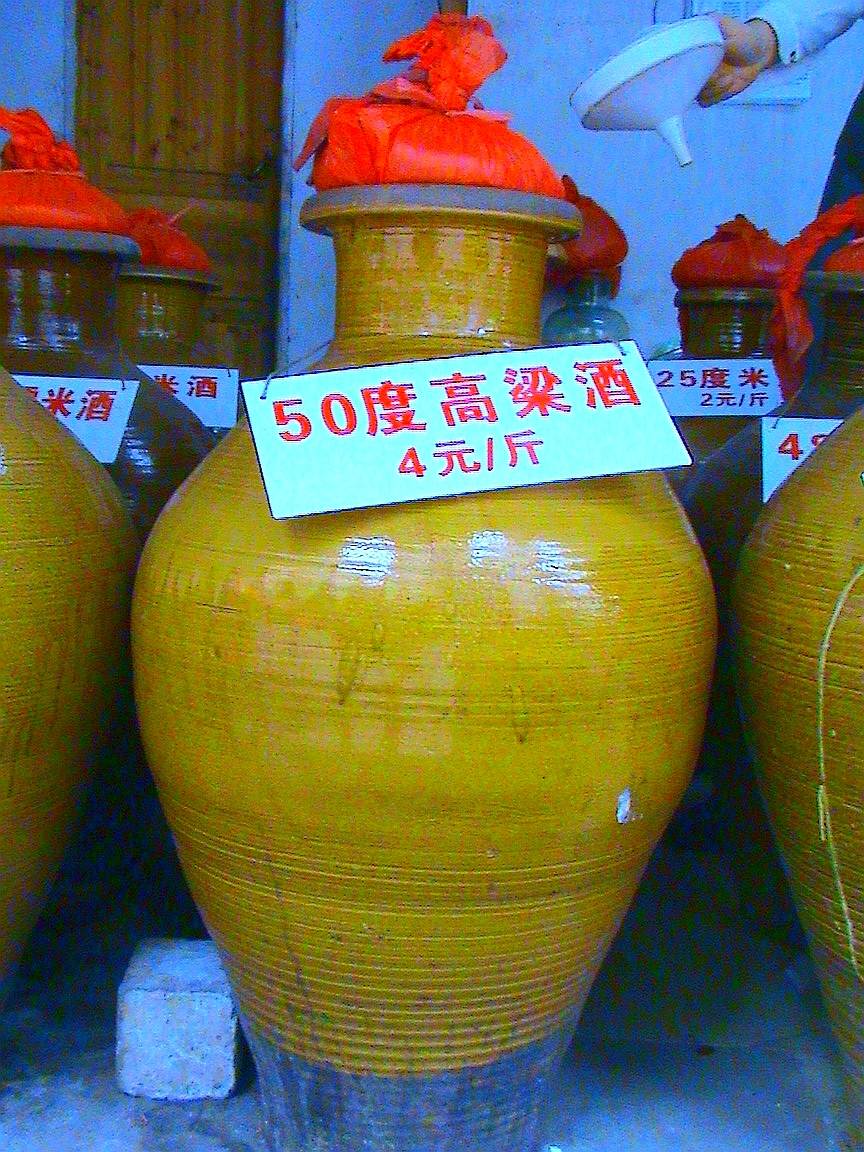 Ceramic jars of sorghum liquor at a market, with handwritten price signs.